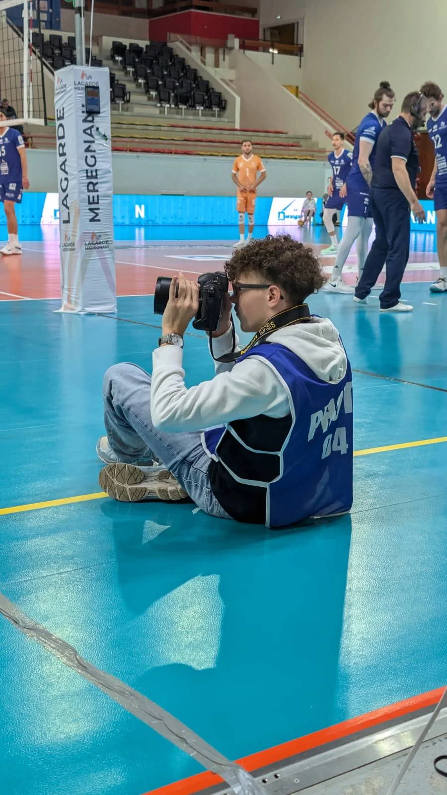 Noan, appareil en main, au bord du terrain pendant un match de volleyball